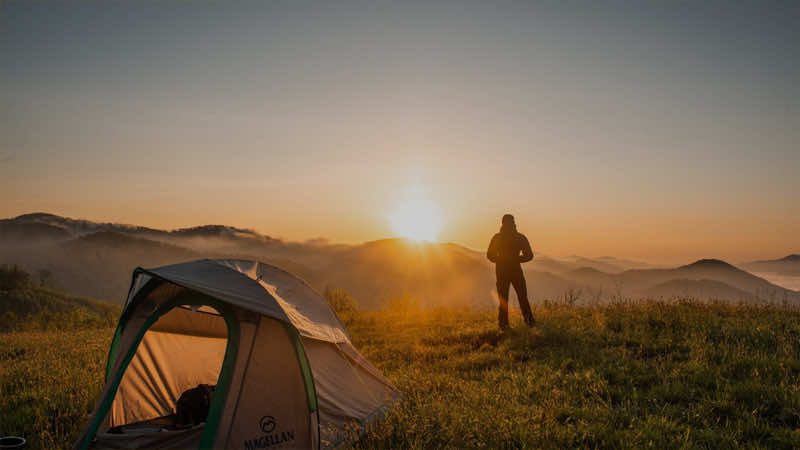 Camper standing solo outside of their tent looking at the mountains